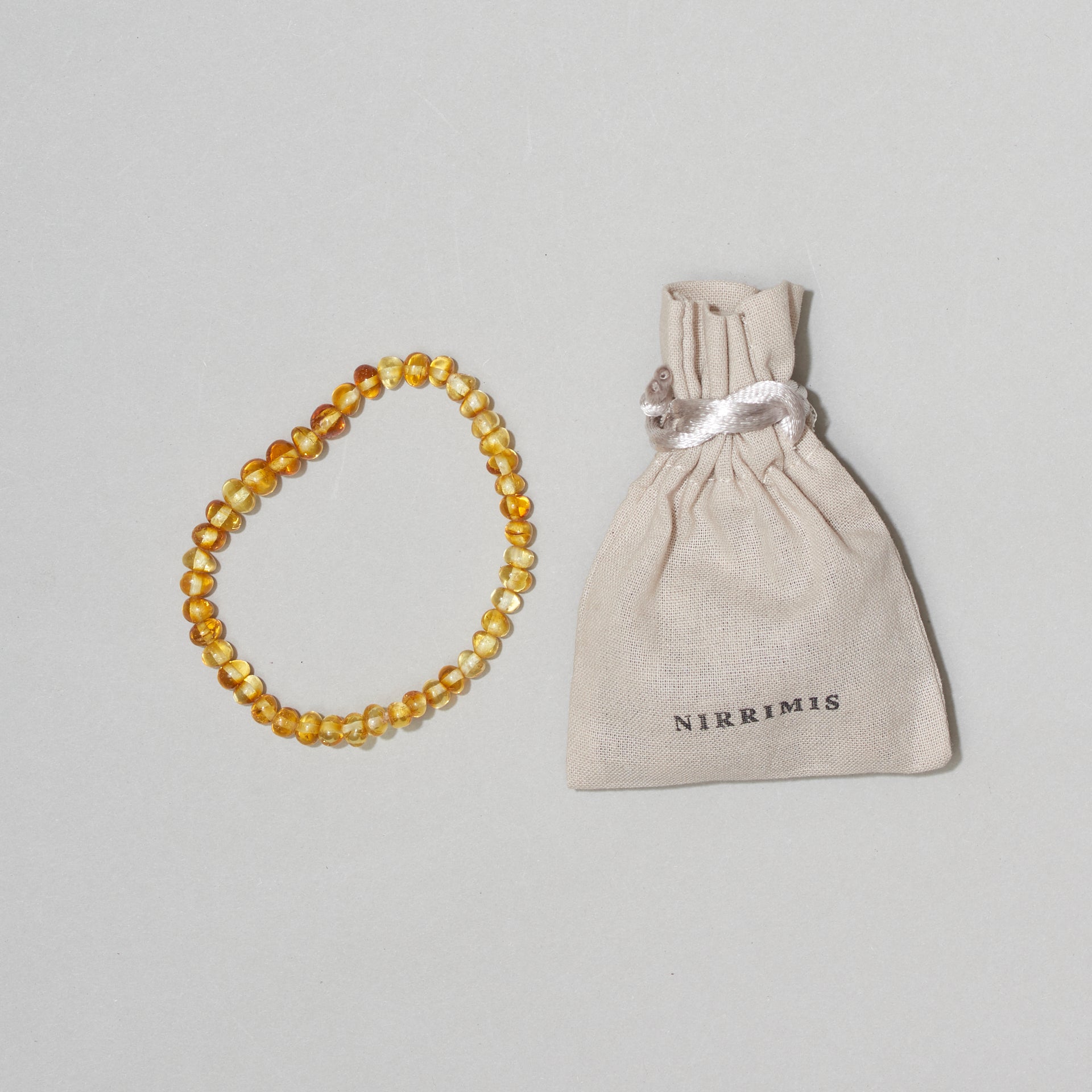 Bernstein-Armkette „Faye“ von Nirrimis, handgefertigt aus echtem Bernstein, elastisch, auf hellem Hintergrund mit Leinenbeutel.