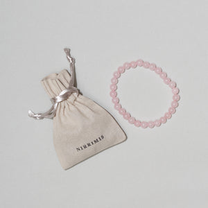 Bernstein-Armkette „Rose Quarz“ von Nirrimis aus baltischem Bernstein und Rosenquarz, elastisch, handgefertigt, auf hellem Hintergrund mit Leinenbeutel.